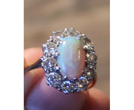 A precious opal and diamond cluster ring, set oval cabochon opal to centre bordered by ten round brilliant cut diamonds withi