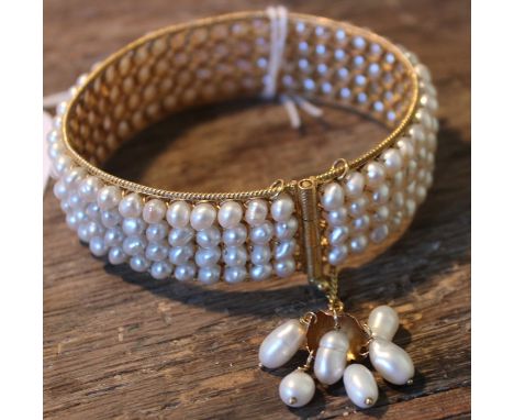 A precious yellow metal and pearl bangle, set four rows of pearls within wire work border, with curb link chains to clasp sus