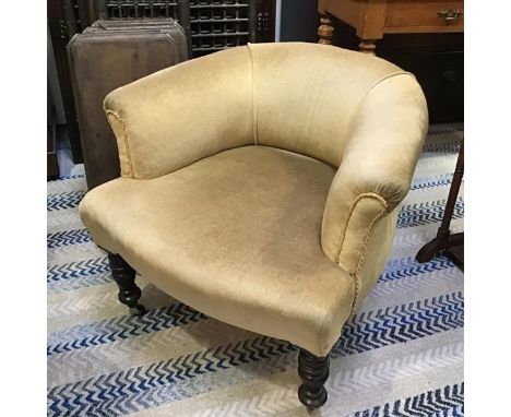 An Edwardian ebonised low back nursing chair with upholstered panel back and seat in gold velour, raised on ring turned suppo