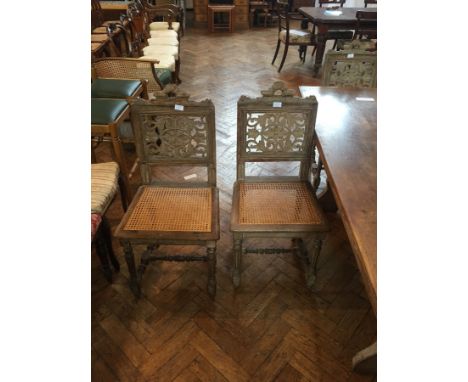 A set of six limed oak dining chairs with foliate carved panel backs and cane seats on carved tapering fluted legs united by 