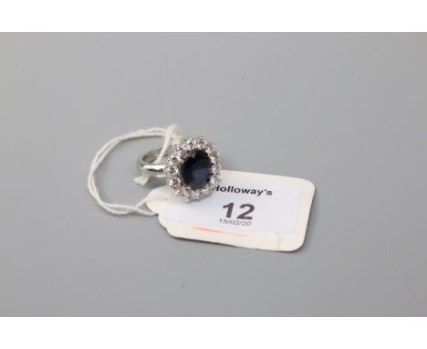 A sapphire cluster ring, the large oval cut sapphire, within a border of clear stones, to a basket style mount, marked '750',