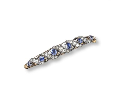 An Edwardian sapphire and diamond hinged bangle, set with six graduated circular-cut sapphires divided with scrolls of gradua