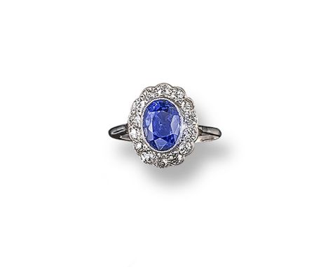 A sapphire and diamond cluster ring, the oval-shaped sapphire is millegrain-set within a surround of cushion-shaped diamonds 