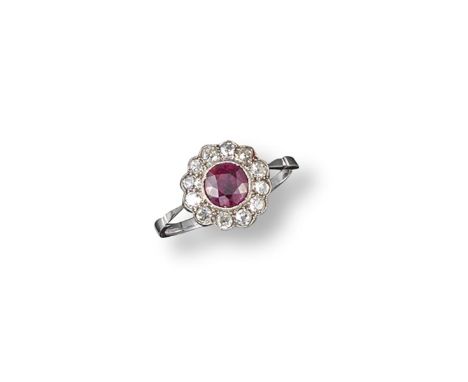 A ruby and diamond cluster ring, the circular-cut ruby is set within a surround of old circular-cut diamonds in platinum and 