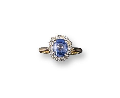 A sapphire and diamond cluster ring, the oval-shaped sapphire is set within a surround of round brilliant-cut diamonds in yel