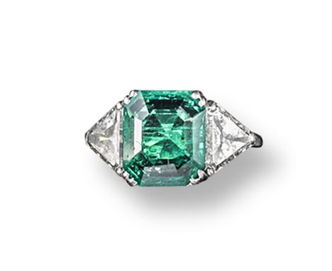 The property of a titled Lady.  An emerald and diamond three stone ring, the emerald-cut emerald is set with two triangular-c