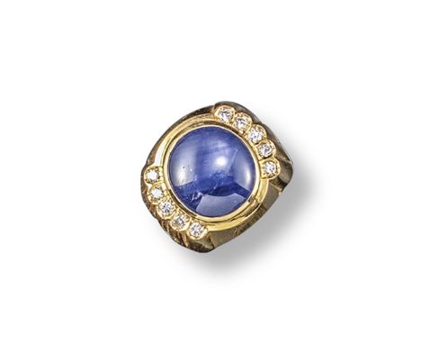 A cabochon sapphire and diamond ring, the slightly oval-shaped sapphire is set within borders of ten circular-cut diamonds in