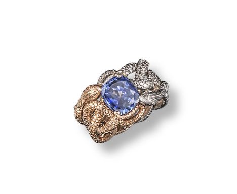 A yellow and white gold double snake ring, realistically formed and mounted with a cushion-shaped sapphire. Size R.