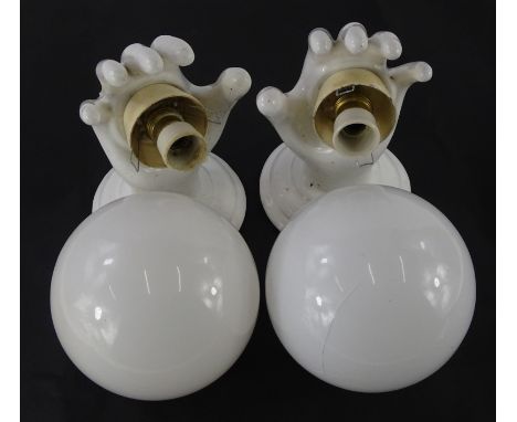 An unusual pair of ceramic wall lights, each modelled in the form of a hand, with opaque globe shaped shades.