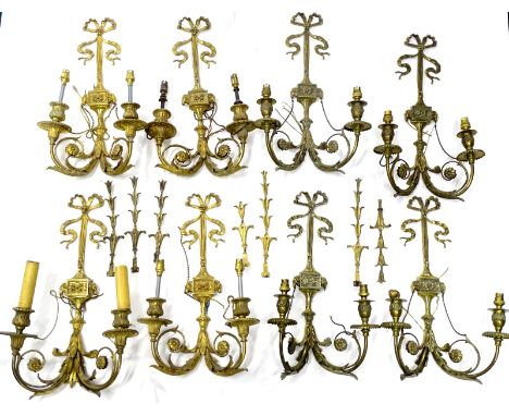 An associated set of eight Louis XVI style gilt metal two branch wall lights, each decorated with ribbons, rams heads and lea
