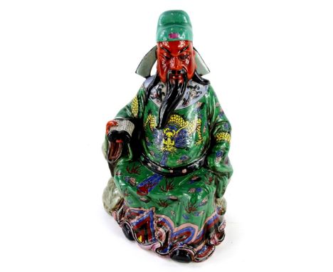 A Chinese porcelain figure of an emperor or immortal, holding a scroll, decorated in yellow, green, blue, purple coloured ena