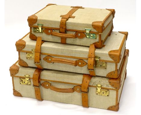 A graduated set of three canvas and brown leather vintage suitcases, the largest 73cm wide, smallest 47cm wide. 