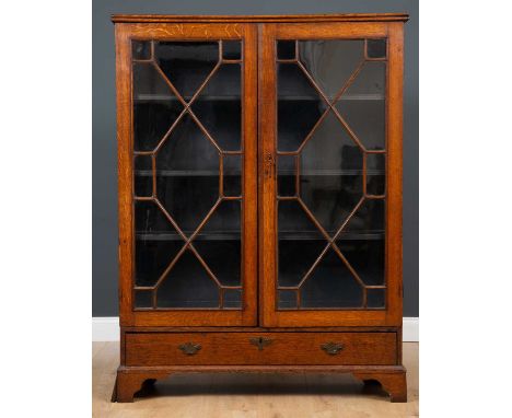 A Georgian oak bookcase with twin astragal glazed doors, three adjustable shelves above a single drawer, raised on bracket fe