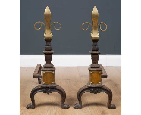 A pair of Victorian brass and cast iron fire dogs, with embossed fleur-de-lis form finials on curved brackets with paw feet, 