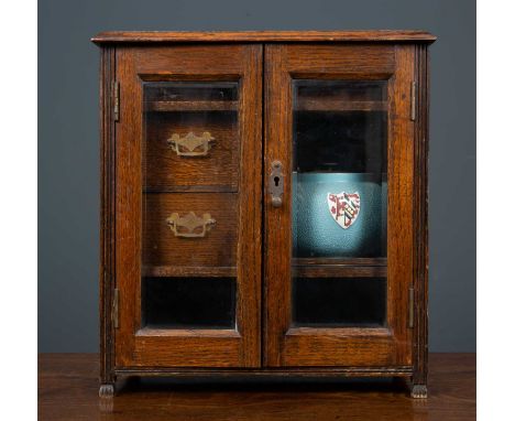 A late 19th / early 20th century oak tobacco cabinet with two glazed doors, a cigar drawer, two short drawers and a Carltonwa