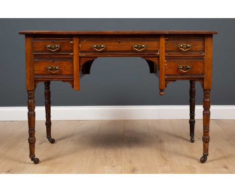 An Edwardian rosewood five drawer writing table with brass handles and turned feet, raised on ceramic casters, 109cm wide x 5