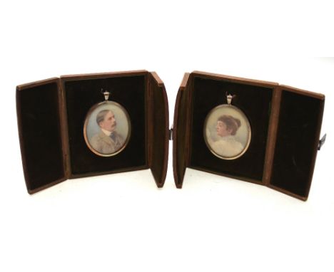A pair of Edwardian oval portrait miniatures on ivory of a husband and wife, unsigned, 6.5 x 5.5 cm, in silver pendant frames