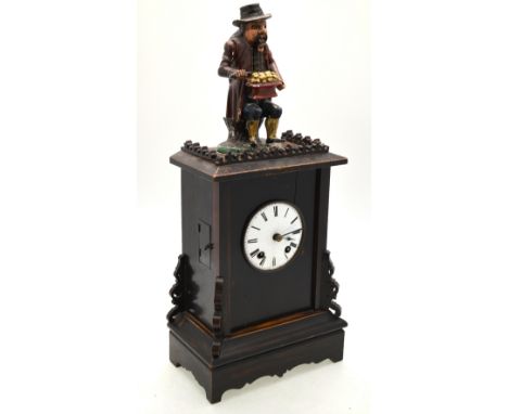 A continental mantel clock surmounted by a polychrome carved wooden seated figure of a bun eater, 55 cm high overall