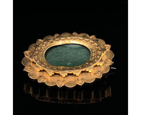 A 15ct GOLD OVAL PANEL BROOCH. A FLARED BORDER WITH A HEART DESIGN FRAMES A GLAZED PERSPEX PANEL TO FRONT AND REVERSE, FITTED
