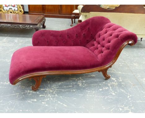 A VICTORIAN MAHOGANY CHAISE LONGUE WITH BUTTONED PLUM VELVET BACK AND SCROLL END, THE SPLAY LEGS ON WHITE CERAMIC CASTER FEET