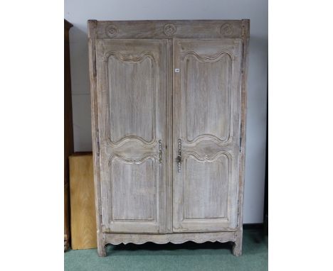 A 19th C. FRENCH LIMED OAK ARMOIRE, THREE ROSETTE ROUNDELS CARVED ABOVE TWIN PANELLED DOORS AND A WAVY APRON RUNNING INTO THE