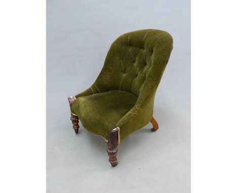 A GREEN VELVET BUTTON BACKED VICTORIAN CHAIR ON MAHOGANY FRONT LEGS CARVED WITH CABOCHONS AND ON BRASS CASTERS 