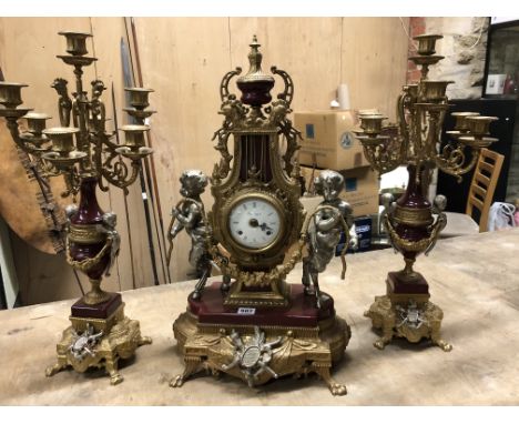 AN ITALIAN IMPERIAL GILT BRASS AND RED CERAMIC CLOCK GARNITURE, THE ENAMEL DIAL IN A LYRE SHAPED CASING SUPPORTED BY TWO SILV