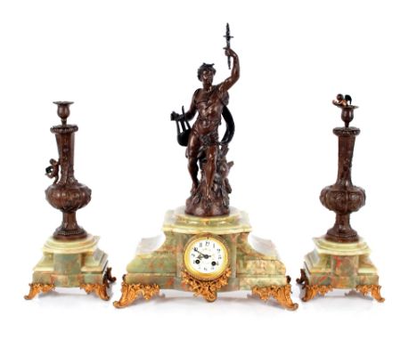 A green marble and spelter clock garniture,&nbsp;the clock surmounted by a figure holding a torch aloft, circular floral enam