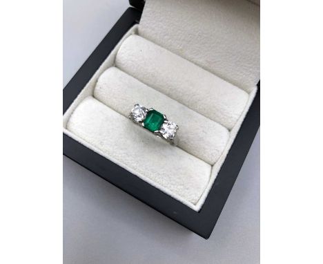 A vintage emerald and diamond three-stone ring. The central emerald in a four-claw setting, approximate measurements 6.4 x 5.