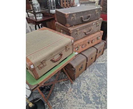 A group of vintage luggage and a folding bridge table.