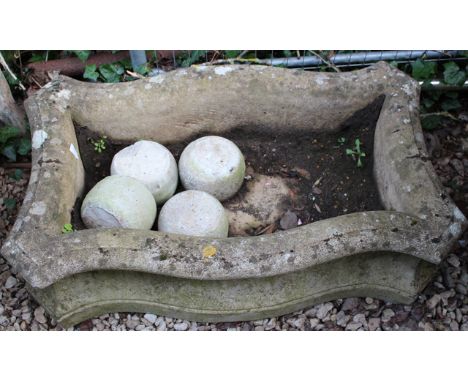 A RECTANGULAR SERPENTINE RECONSTITUTED STONE SHALLOW GARDEN PLANTER with concave sides and standing on four bun feet, 91cm wi