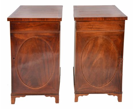 A PAIR OF REGENCY AND LATER MAHOGANY CABINETS with crossbanded tops, the oval paneled doors opening to reveal drawers within,