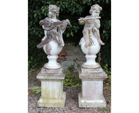 A PAIR OF CONCRETE SCULPTURES DEPICTING PUTTI RESTING ON BALL FINIALS,  one playing a lute and the other a flute, 98cm high, 