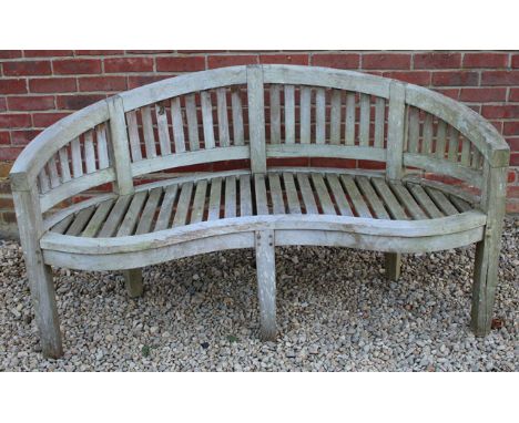 A WEATHERED TEAK GARDEN BENCH with a curved back and serpentine seat, 150cm wide