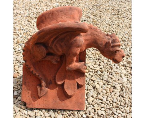 A CAST TERRACOTTA COLOURED DRAGON ROOF RIDGE FINIAL, a dragon crouching on a triangular ridge tile, 51cm long x 47cm high 