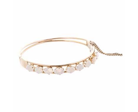 A 14CT GOLD AND OPAL BANGLE of circular hinged form, embellished to the centre with oval cabochon opals, with safety chain, i