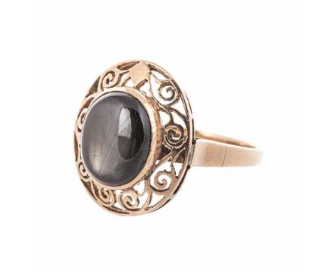 A GOLD RING centred with an oval cabochon black stone, within a conforming surround of scrolls, impressed 18K, size O 