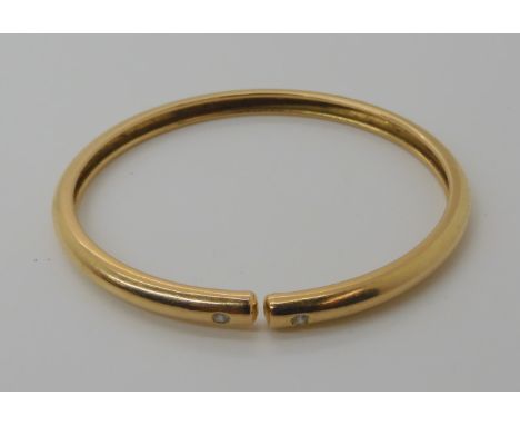 An 18ct gold bangle set with two 0.04ct brilliant cut diamonds, approx diameter 6cm, weight 11.7gms Condition Report: This ba