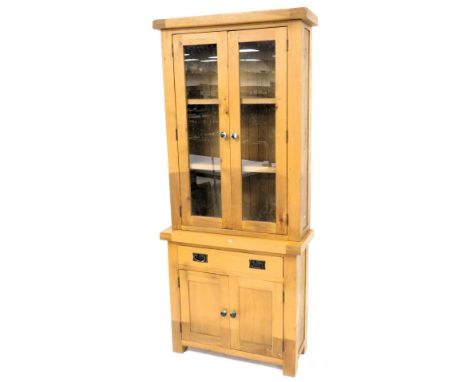 A light oak cabinet, the top with two glazed doors, the base with a drawer and two panelled doors, on stiles, 201cm high, 85c