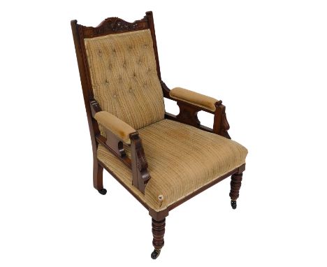 A Victorian walnut nursing chair, upholstered in light brown button back fabric, raised on turned legs, brass capped on casto