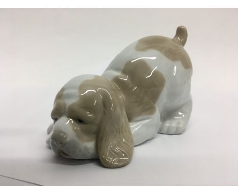 A Nao figurine of a spaniel type dog with lowered head and sad expression.