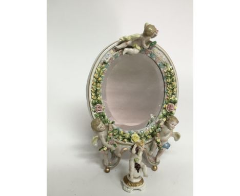 A continental porcelain mirror framed with cherubs and a small figure of similar type