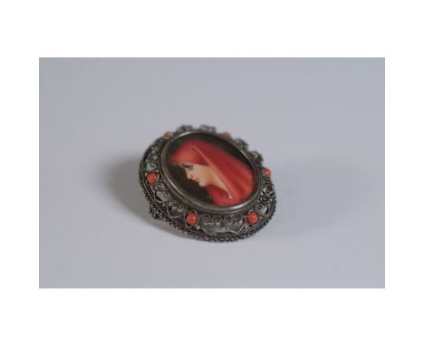 This elegant oval brooch, marked 800 for silver content, features a painted portrait of a woman in a red veil encased in glas