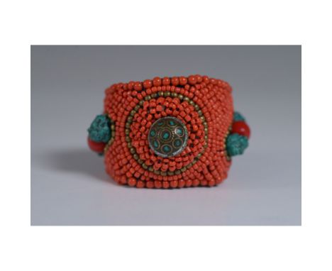 A vibrant handcrafted cuff bracelet featuring intricate beadwork in bold orange hues, accented by brass-toned beads and turqu