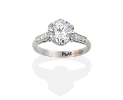 A Diamond Solitaire Ring, the round brilliant cut diamond in a white six claw setting, to pointed shoulders inset with single