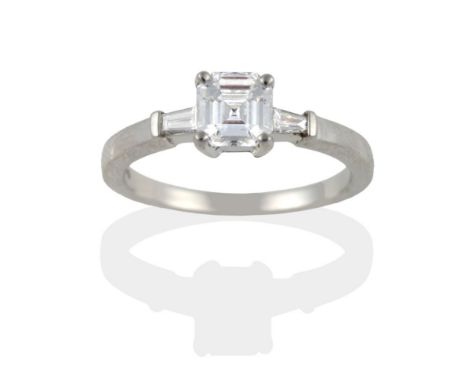 A Platinum Diamond Ring, the octagonal step cut diamond in four claws, to tapered baguette cut diamond shoulders on a plain p