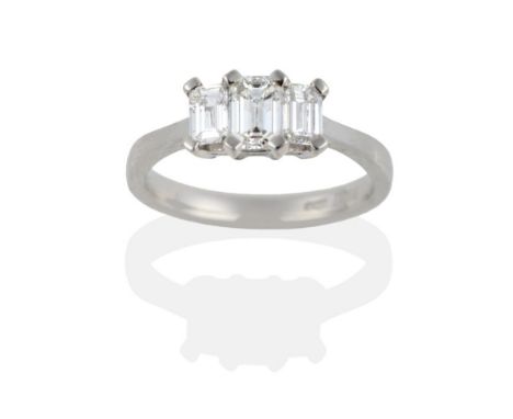 A Platinum Diamond Three Stone Ring, the emerald-cut diamonds in claw settings on a tapered shoulder plain polished shank, to