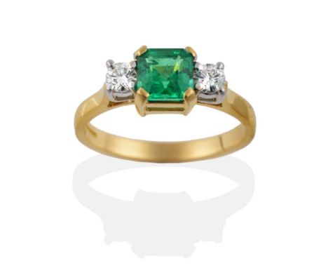 An 18 Carat Gold Emerald and Diamond Three Stone Ring, the octagonal step cut emerald in four yellow claws, flanked by two ro