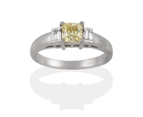 A Platinum Diamond Three Stone Ring, the yellow princess cut diamond in a four claw setting to baguette cut diamond shoulders