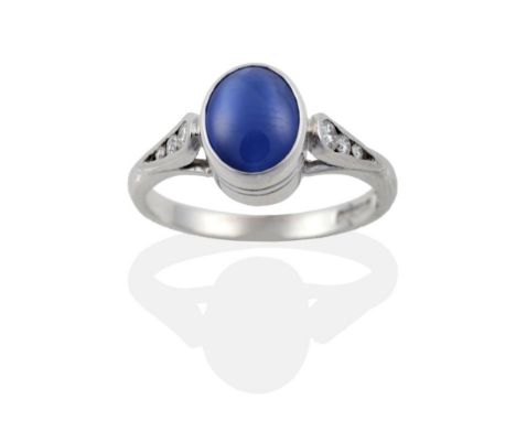 An 18 Carat White Gold Star Sapphire and Diamond Ring, the oval cabochon star sapphire in a rubbed over setting, to shoulders